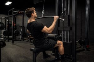 Man performing lat pulldown exercise on a cable machine in a commercial gym to build upper back strength, improve pulling power, and support the big three powerlifting lifts performance with targeted accessory training.