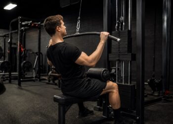 Man performing lat pulldown exercise on a cable machine in a commercial gym to build upper back strength, improve pulling power, and support the big three powerlifting lifts performance with targeted accessory training.