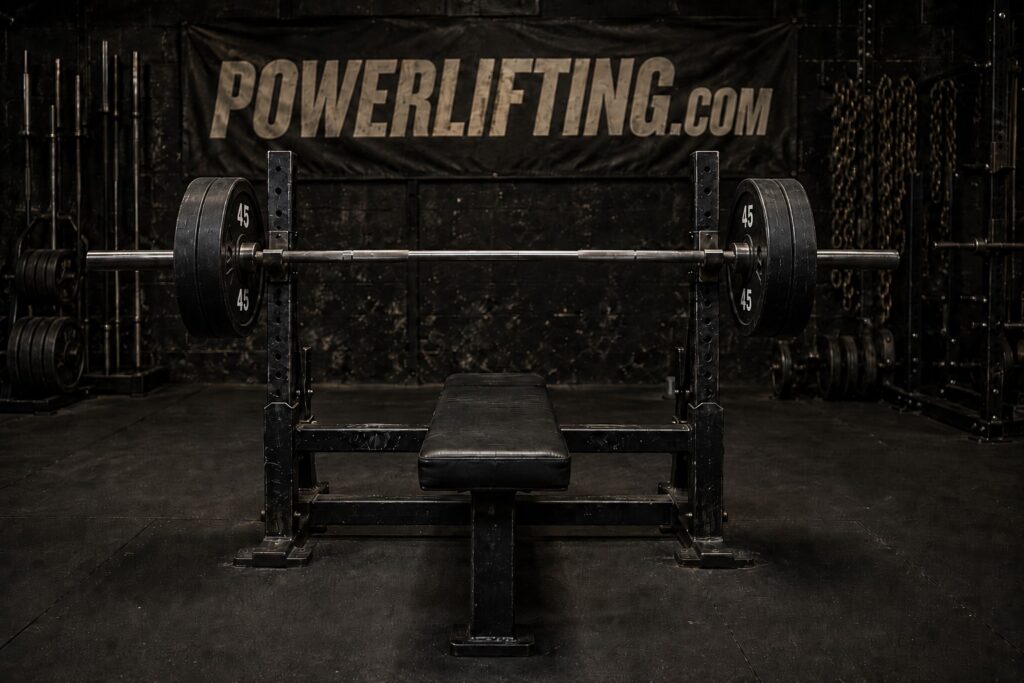 Powerlifting bench press setup with a loaded Olympic barbell on a flat bench inside a strength training gym, showcasing heavy weightlifting equipment for bench press training, powerlifting workouts, upper body strength, and competition preparation.