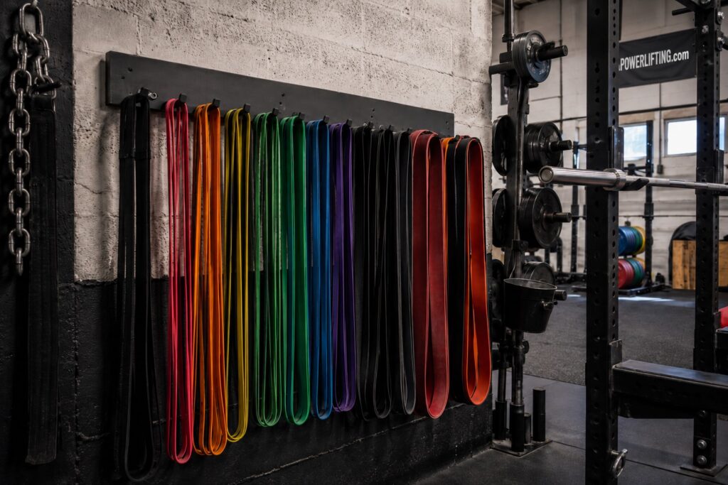Resistance bands organized by color and tension level in a powerlifting gym, used for strength training, mobility exercises, and accommodating resistance.