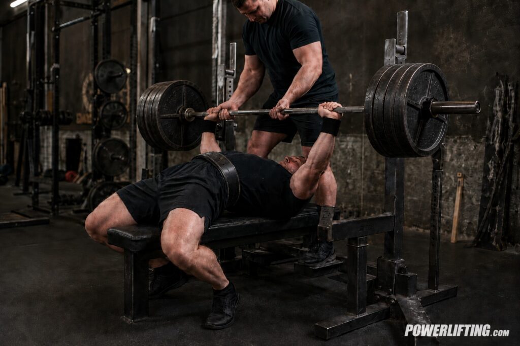 Powerlifter setting up for a heavy bench press with a spotter, showing how tightness, position, and control start before the bar moves.