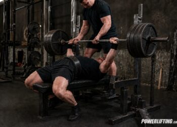 Powerlifter setting up for a heavy bench press with a spotter, showing how tightness, position, and control start before the bar moves.